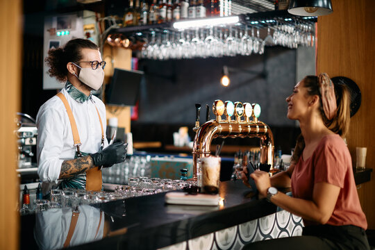 Happy barman wears protective face mask while serving customer in pub during coronavirus pandemic.