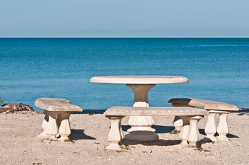 front view, medium distance of a concrete tables and three concrete benches on a sandy, tropical beach close to the shoreline