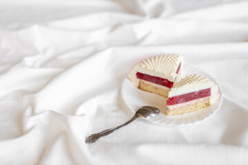 A white-pink piece of cake lies on a white plate on a light background. Delicious pastries