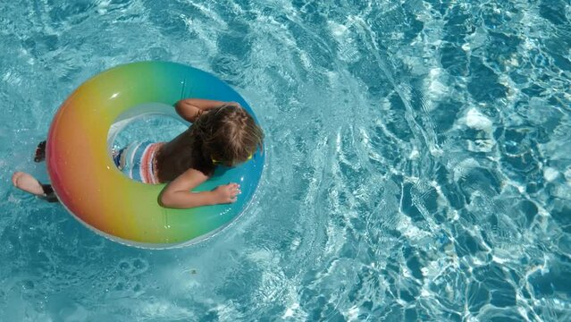 Happy kid playing with colorful swim ring in swimming pool on summer day. Children playing in the swimming pool. Summer activity.