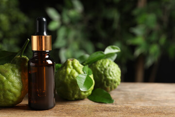 Glass bottle of bergamot essential oil and fresh fruits on wooden table. Space for text - obrazy, fototapety, plakaty