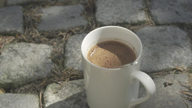 Mug with a natural black warm coffee stands on a cobblestone. Autumn In the background.