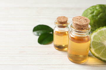 Glass bottles of bergamot essential oil on white wooden table, closeup. Space for text