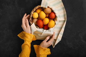 Female hands and wicker basket with painted Easter eggs on dark background