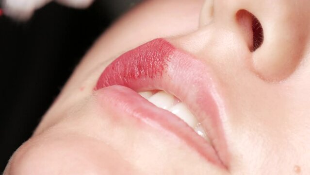 Microblading lip tattoo with special coloring red pigment that corrects lip color in cosmetology clinic. Permanent makeup lips procedure applying pigment makeup on lips with a tattoo machine close up