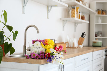 Modern light kitchen with bouquet of flowers in sink