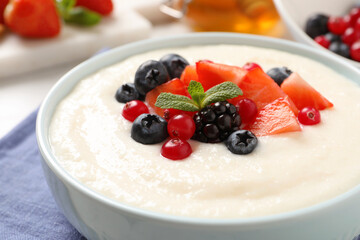 Delicious semolina pudding with berries in bowl on table, closeup