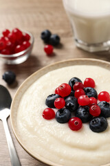 Delicious semolina pudding with berries in bowl on table, closeup
