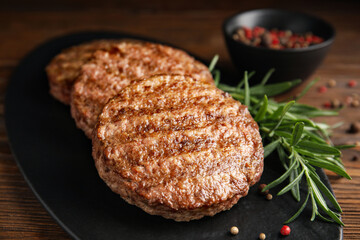 Slate plate with tasty grilled hamburger patties and seasonings on wooden table, closeup