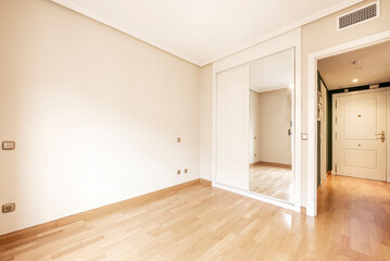 Empty room with a built-in wardrobe with sliding doors and a white window through which a lot of light enters