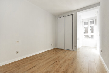 Empty room with a built-in wardrobe with sliding doors and a white window through which a lot of light enters