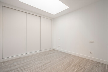 Angular view of a built-in wardrobe with white sliding doors and imitation wood stoneware floors...