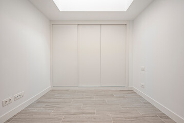 Front view of a built-in wardrobe with white sliding doors and wood-look stoneware floors