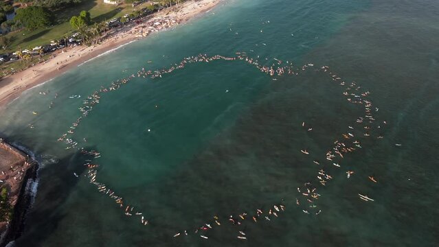 Aerial shot of group of surfers paddle out in the transparent ocean