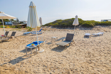 Close up view of empty sun beds och closed sun umbrellas on sand beach. Greece.  - obrazy, fototapety, plakaty
