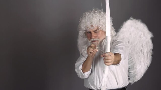 Funny cupid, handsome guy on valentine day with bow arrow shooting. Love concept. Handsome crazy fun angel. Bearded valentin man with angel wings.
