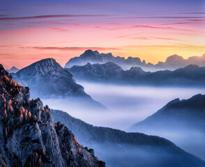 Fototapety  Mountains in fog at beautiful sunset in autumn in Dolomites, Italy. Landscape with alpine mountain valley, low clouds, trees on hills, colorful sky at dusk. Aerial view. Passo Giau at night. Nature