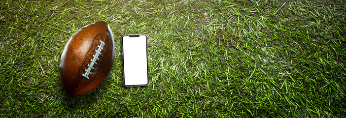 smartphone and american football ball on the grass of a stadium