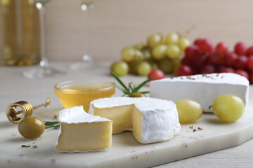 Tasty brie cheese with olives and grapes on white board