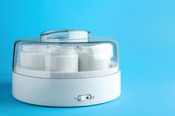 Modern yogurt maker with full jars on light blue background