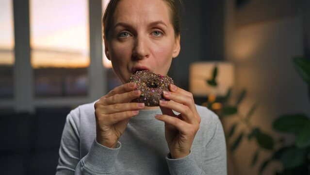 Sweet addiction concept. Woman eats chocolate donut with morbid rapture.