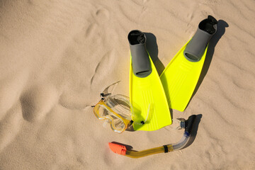 Pair of flippers, snorkel and diving mask on sandy beach, flat lay. Space for text