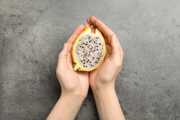 Woman holding fresh cut dragon fruit (pitahaya) on grey table, top view