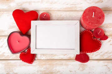 Photo frame between Valentines day romantic decoration with heart and candle on a white wooden table. Top view, copy space.