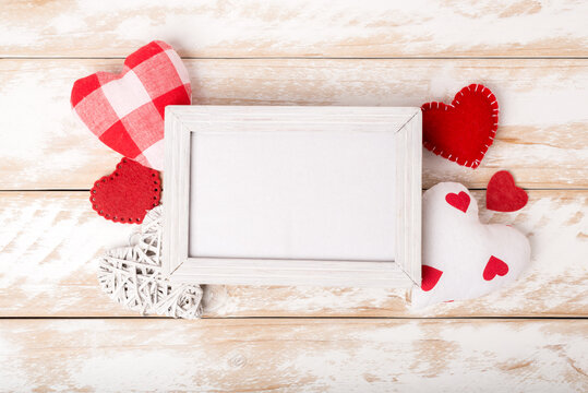 Photo frame between Valentines day romantic decorating with various hearts on a white wooden table. Top view, copy space.