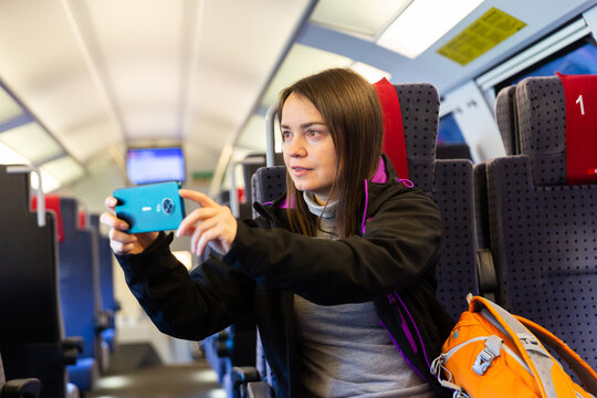 Woman using her smartphone to photograph view from train window.