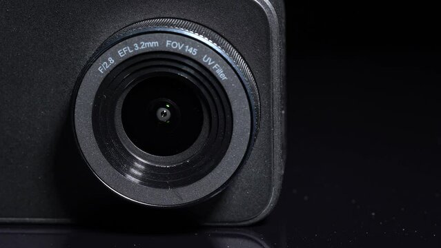 Generic 4k action camera macro close up selective focus. Rotation of simple modern small video camera lens at black background. Vlogger social media and influencer cam concept.