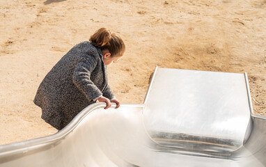 Little girl leaning on the edge of a playground slide.