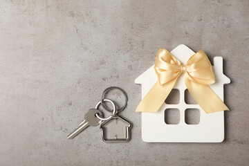 Wooden house model, bow and key on grey table, flat lay with space for text. Housewarming party