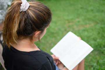 Top view of a young caucasian woman reading a book in a park.
