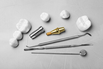 Post, abutment and different crowns of dental implant near medical tools on grey table, flat lay