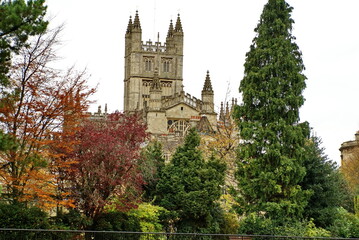 Bath Abbey surrounded by autumn foliage in Bath, England, seen from the bank of the River Avon
