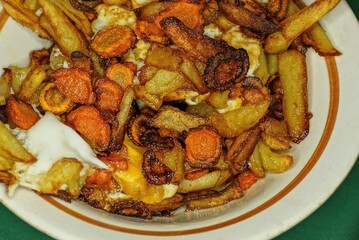 food of fried potatoes with carrots and scrambled eggs in a white plate on a green table