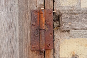 one red iron old rusty door hinge on a gray door board outside