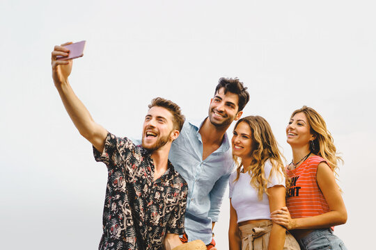 reunion gathering of generation z people having fun taking smartphone's selfie outdoors - isolated on white sky background - vacation and summer friendship carefree concept - vivid color filter