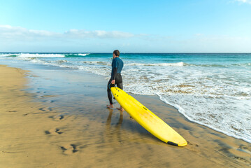 A surfer with a surfboard walks along the sandy beach of the ocean 