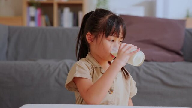 Slow motion - Portrait of cute asian little girl drinking milk sits at the living room. Child with a glass of milk before breakfast. children healthy concept.