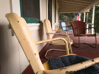 Vintage, metal armchairs on outdoor covered porch of cabin. Faded yellow and burgundy chairs with...