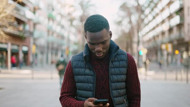 Black man browsing smartphone and walking in city
