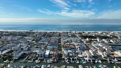 Aerial riser shot over a coastal beach city neighborhood with beautiful coastline, sea, waves and sand below on a sunny day with luxury homes.