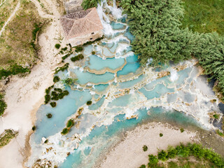 Aerial view of Terme di Saturnia, geothermal sulfur springs and natural spa with waterfalls at Saturnia thermal baths. People batching at Cascate del Mulino, Tuscany, Italy.