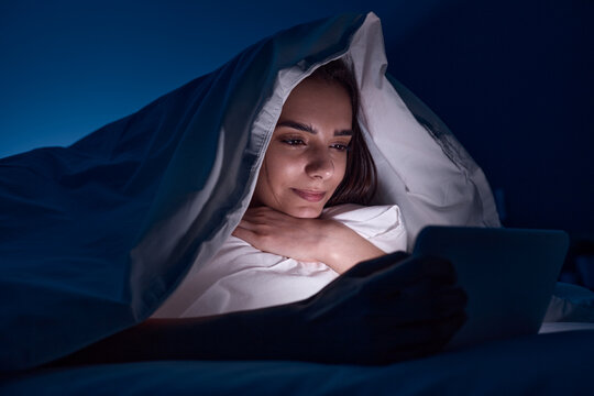 Woman watching movie in bed at night