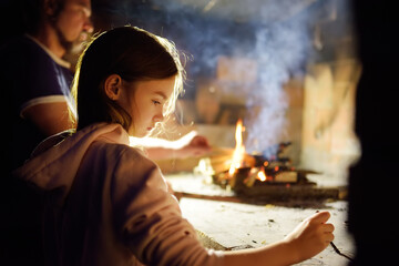Adorable young girl roasting marshmallows on stick at bonfire. Child having fun at camp fire....