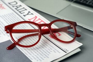 Newspaper, laptop and glasses on grey table, closeup