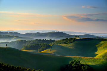 Stunning morning view of fields and farmlands with small villages on the horizon. Rural landscape of rolling hills, curved roads and cypresses of Tuscany, Italy.