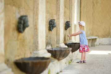 Little girl playing with a drinking water fountain in Sorano, an ancient medieval hill town hanging...